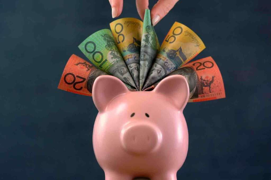 A ceramic pink Piggy bank money concept on dark blue background, stuffed with Australian cash, and female hand take one hundred dollar note.